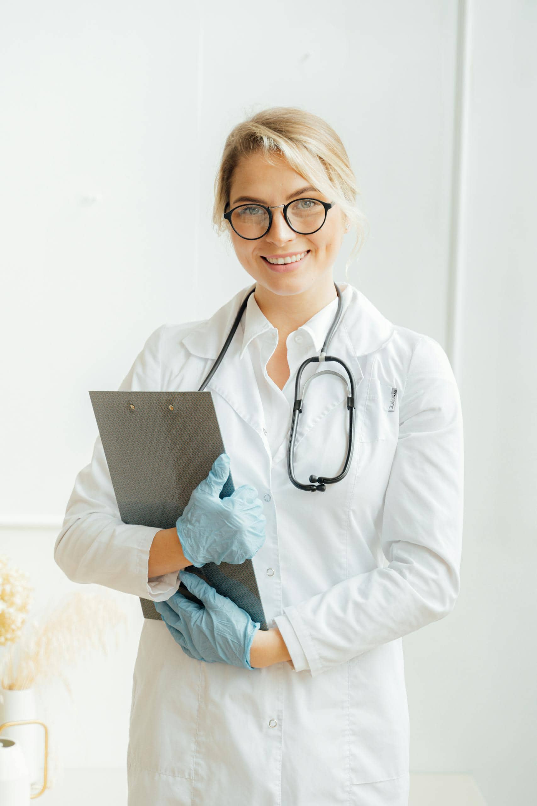 Portrait of a smiling female doctor in a lab coat with stethoscope and clipboard indoors.
