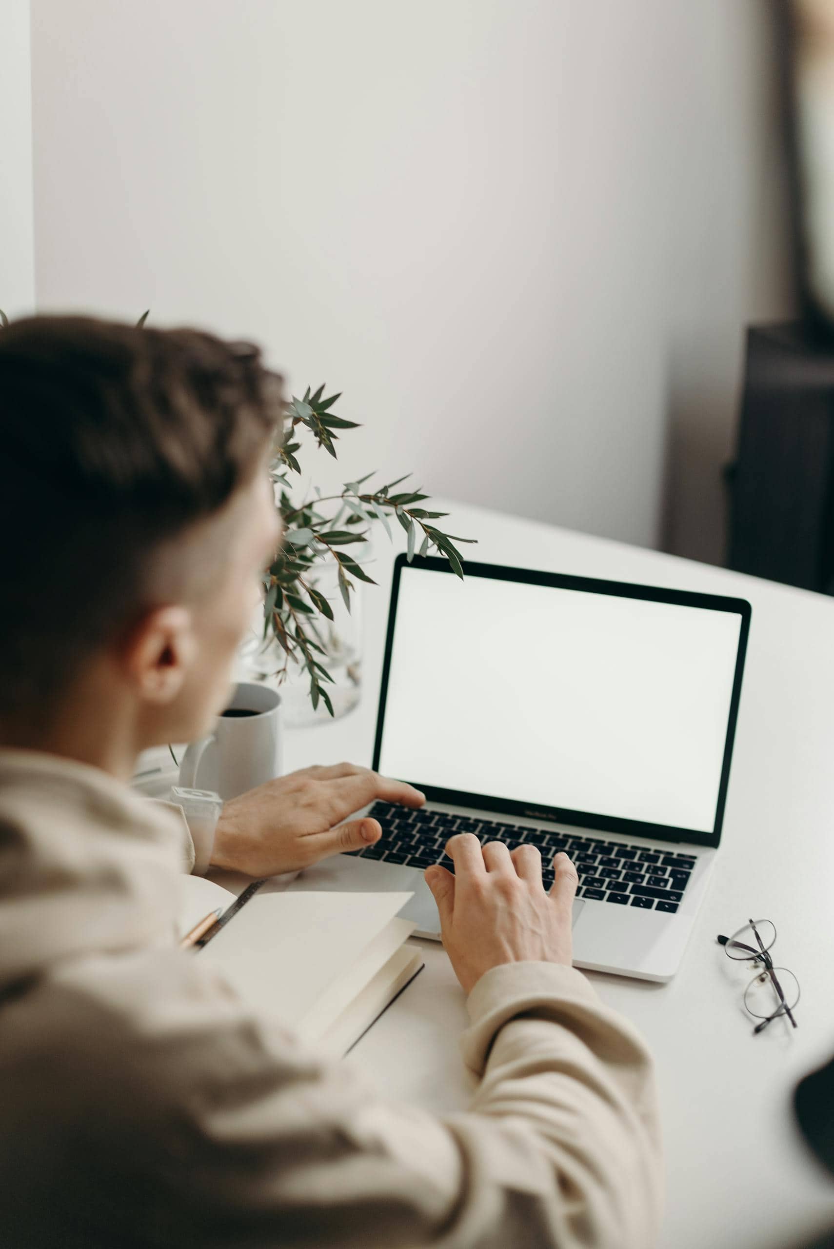 Young man typing on a laptop at a clean, minimalist desk with a plant.