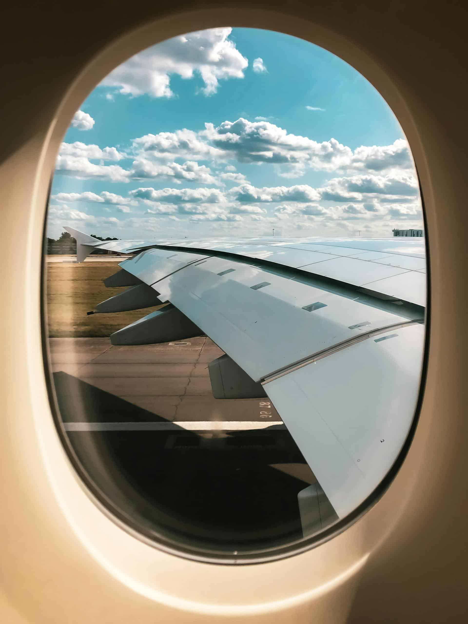 View of airplane wing and cloudy sky from passenger window, showcasing in-flight travel experience.